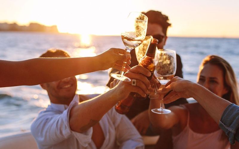 Grupo de amigos brindando en un barco al atardecer en Ibiza, con el mar y la luz dorada del Mediterráneo como fondo.